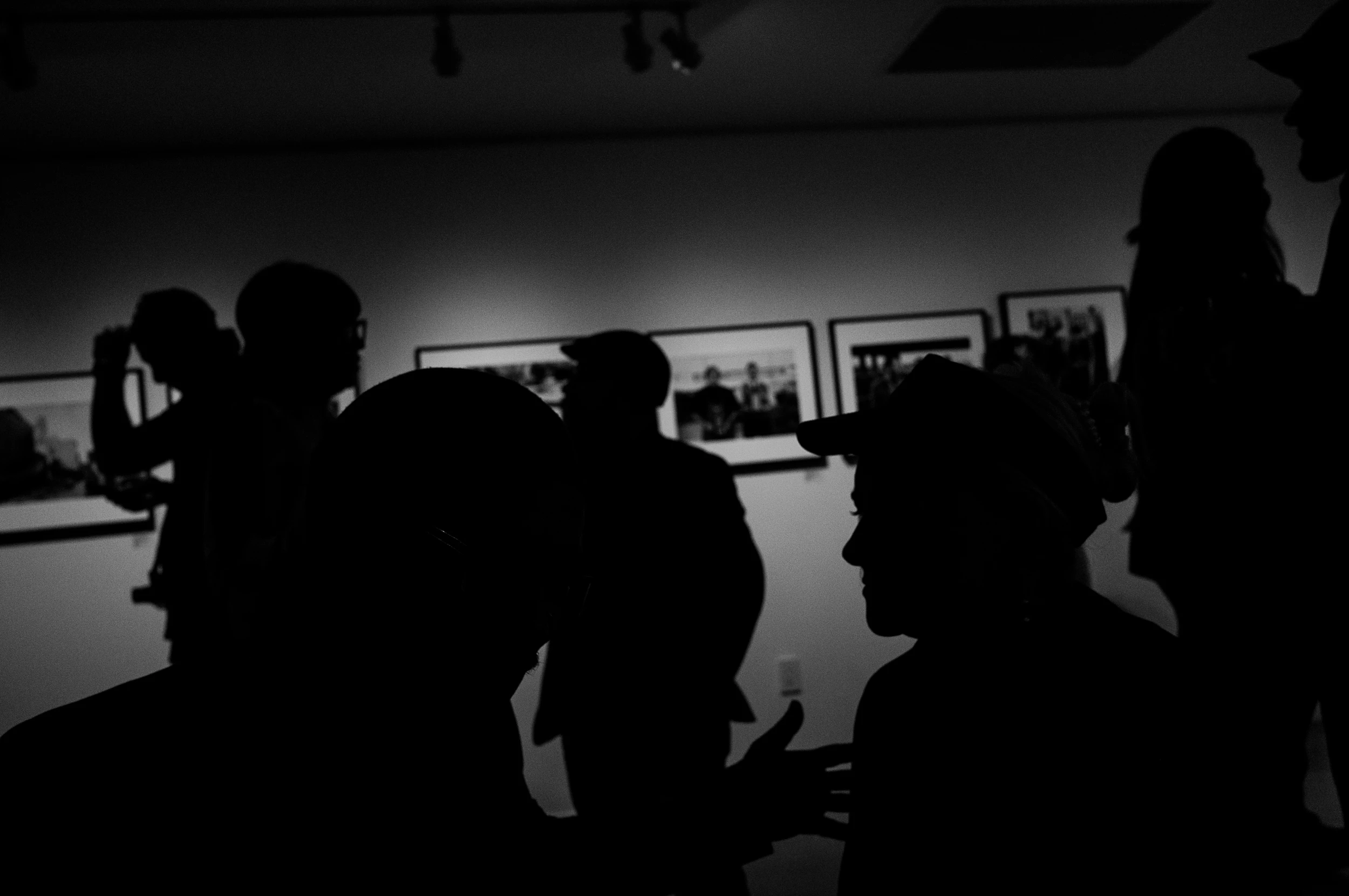 Black-and-white silhouettes of people viewing photographs in a gallery