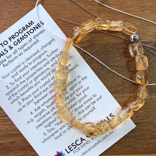Citrine bracelet that has been restrung by Lesca Crystals resting on timber table and Lesca Crystals Programming/Intention Card.