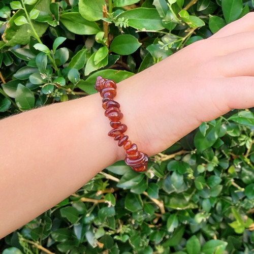 Hessonite Garnet Premium Chip Bracelet on hand of a chil against jasmine green hedge background