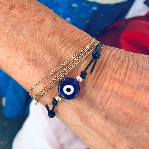 Lampwork Blue Evil Eye Cowhide Cord Bracelet with gold figaro chains on coloured background
