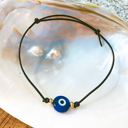 Lampwork Evil Eye Cowhide Cord Bracelet resting on a large shell