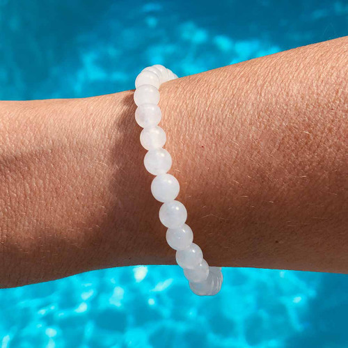 Hand wearing a White Jade 8mm bead bracelet with water behind