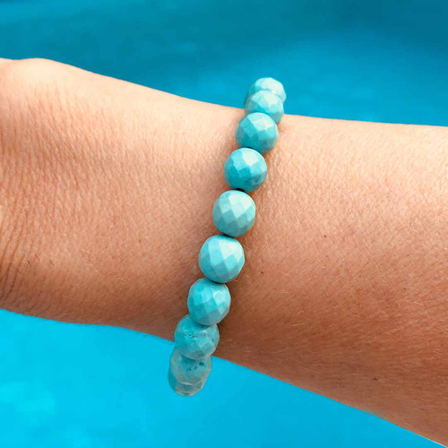 Hand showcasing Aqua Blue Magnesite 8mm Faceted Bead Bracelet with water behind