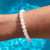 Hand wearing a White Jade 8mm bead bracelet with water behind