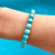 Hand showcasing Aqua Blue Magnesite 8mm Faceted Bead Bracelet with water behind