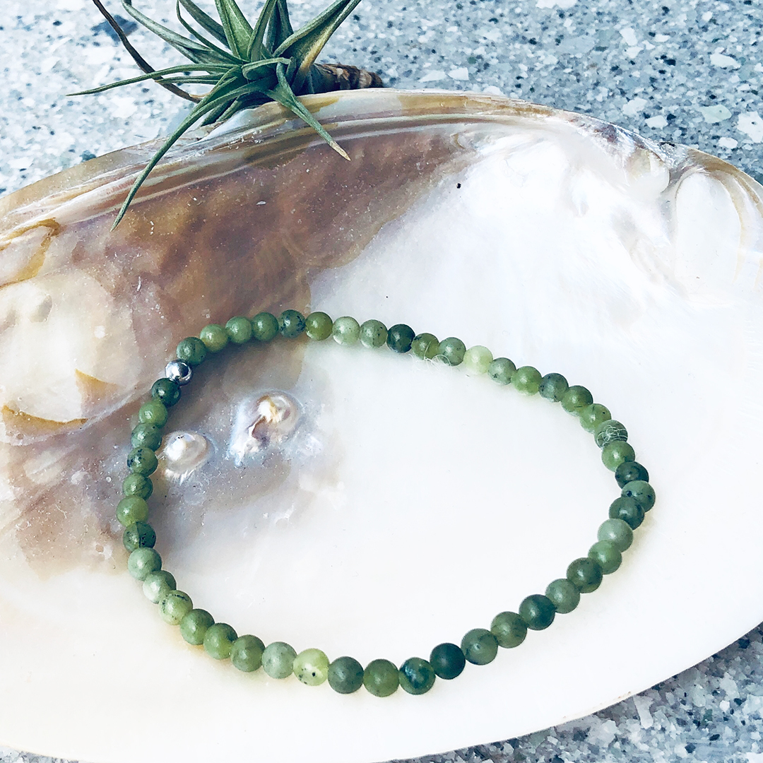 Jade 4mm bracelet on shell with rocks behind