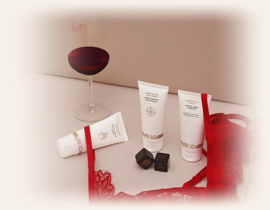 Drie tubes YESforLOV glijmiddel met een glas rode wijn, twee dobbelstenen en rode kanten lingerie