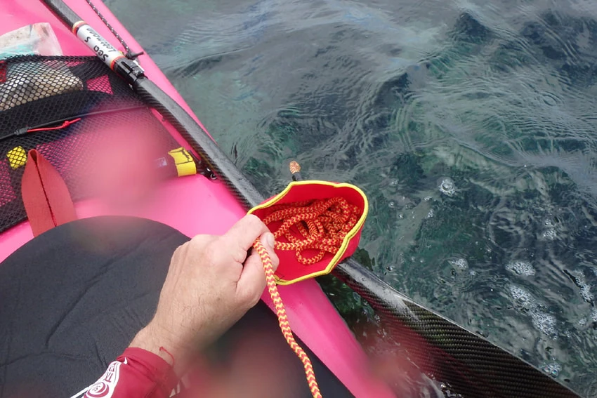 Rescue throwline bag and coiled rope being handled beside a kayak
