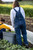 Woman in bib overalls harvesting plants in a field.