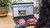 Refurbished Hand touching trackpad on laptop keyboard as screen displays a webpage about electronics, with visible camera and microphone