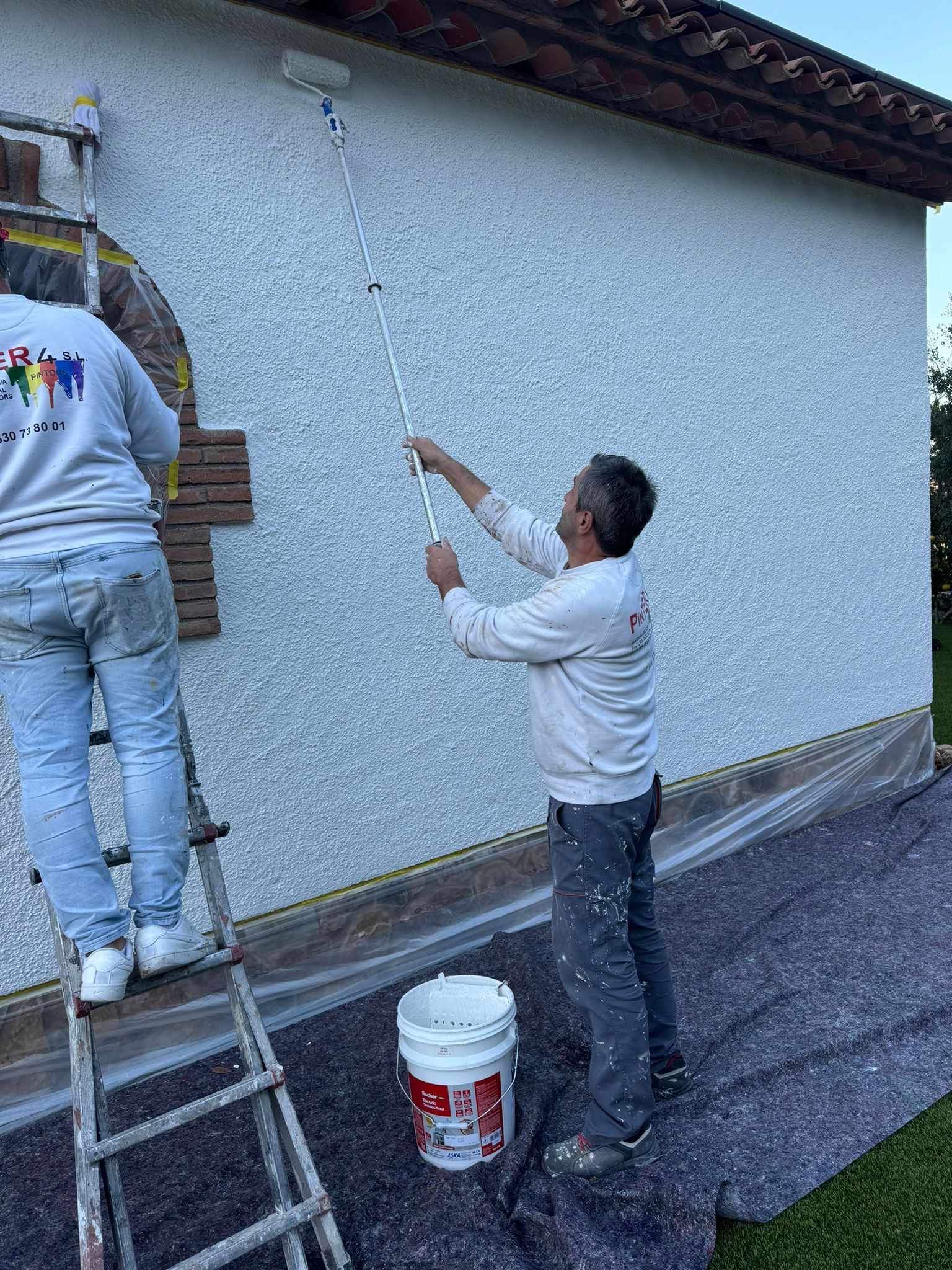 Profesionales aplicando el revestimiento con rodillo sobre una fachada exterior