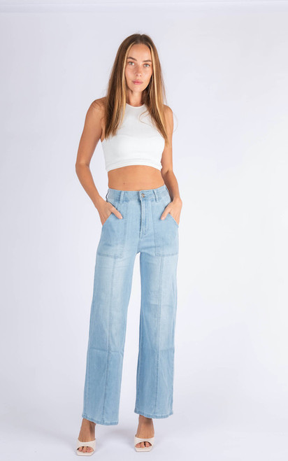 Model wearing the Cassandra high-waisted wide leg jeans in light blue denim, paired with a white sleeveless crop top and white square-toe mules