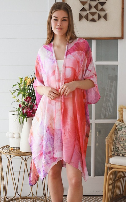 Model wearing the semi-sheer Sunset Blossom kimono. The open-front chiffon kimono features a vibrant mix of coral red, hot pink, magenta, and lavender abstract watercolour shapes layered over a solid white top.