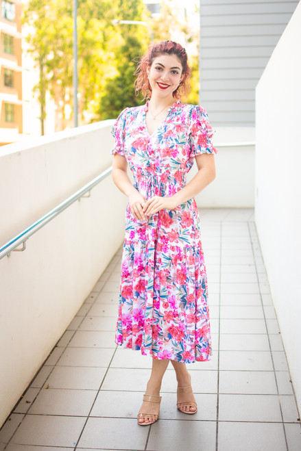 Celebrate your next special occassion in our gorgeous Alexia Floral Midi Dress! Featuring a bright, fun floral print, slightly puffed sleeves with frill, ladder lace details, a shirred waist and pockets, this dress definitely ticks all the boxes! Pair with strappy heels or cute wedges to complete the look.

This dress features:

V-neckline
Button up bust
Short, slightly puffed sleeves with frill detail and shirring
Shirred waist with functional drawstring
Tiered skirt
Shirred detail and frill on neckline
Colour: White with Pink Floral

Fabric: 80% Viscose; 20% Linen

Size Guide: True to size