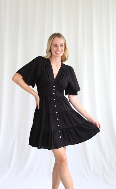 Whether you're going on out to dinner or just a stroll by the beach, our Deborah Dress is sure to impress! She's an easy, throw on and go style in a lightweight fabric that can be easily dressed up or down. Pair with our Tied in Knots Slides for a casual day look or strappy heels for a dinner date.

This dress features:

V-neckline
Button up front
Butterfly sleeves
Textured fabrication
Front panel detail
Shirred waist at the back
Tiered skirt with frilled hemline
Not lined
Colour: Black

Fabric: 100% Rayon

Size Guide: True to size