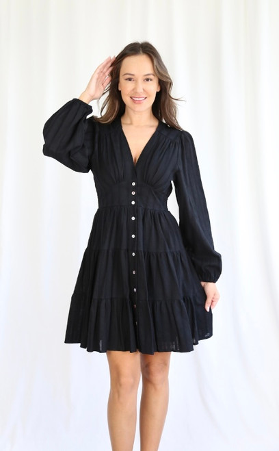 Whether you're going on out to dinner or just a casual lunch, our cotton Amy Dress is sure to impress! She's an easy, throw on and go style that can be easily dressed up or down. Pair with some ankle boots and our Blue Denim Jacket for a casual day look or strappy heels for a dinner date.

This dress features:

V-neckline
Button up front
Long balloon sleeves
Textured fabrication
Front panel detail
Shirred waist at the back
Tiered skirt with frilled hemline
Fully lined apart from sleeves
Colour: Black

Fabric: Outer: 100% Cotton; Lining: 100% Rayon

Size Guide: True to size