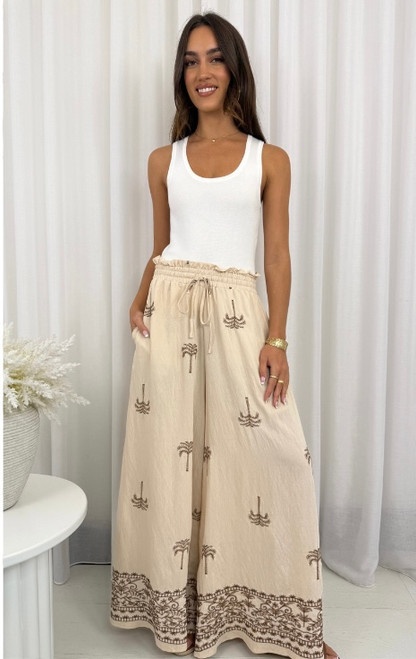 Embrace effortless island vibes in our Palm Breeze Embroidered Wide Leg Pants. Crafted in a lightweight fabric, these beige beauties feature a relaxed silhouette, elasticised waist, and intricate palm tree embroidery for a laid-back luxe look. The stunning border detail adds a boho-chic finish, making them the perfect statement piece for beach strolls, brunches, or your next getaway. Pair with a tank top or cropped blouse and slides for easy resort style.

These pants feature:

Elasticised waist with drawstring
2 side pockets
Full length, wide leg fit
Embroidered detailing
Lightweight
Unlined
Colour: Beige with Tan Embroidery

Fabric: 90% Viscose, 10% Nylon

Size Guide: True to size. Model is wearing a size 8 and is 172cm tall.