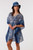 Model wearing the Into The Deep matching resort wear set. The set features a cotton V-neck kaftan cover-up and a matching unstructured bucket hat, both showcasing a rich indigo blue and white botanical leaf pattern with a decorative blue chevron border.