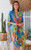 Model wearing the easy, open-front Botanical Oasis kimono. The vibrant cornflower-blue kimono features a bold pattern of large yellow, green and pink tropical flowers, styled over a neutral tank top.