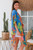 wearing the easy, open-front Botanical Oasis kimono. The vibrant cornflower-blue chiffon cardigan features a bold pattern of large yellow, green, and pink tropical flowers, styled over a neutral tank top.