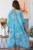 Model wearing the Lagoon Ripple Kimono. The lightweight, semi-sheer sky blue kimono features an abstract ripple print with a thin dark navy border, styled casually over a solid white top and white shorts.