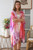 Model wearing the semi-sheer Sunset Blossom kimono. The open-front chiffon kimono features a vibrant mix of coral red, hot pink, magenta, and lavender abstract watercolour shapes layered over a solid white top.