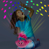 Little girl sitting beside the Trolls Poppy Sleeptime Lite while looking up at the colorful stars projected onto the ceiling.