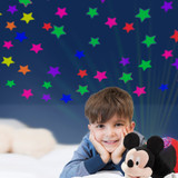 Little boy smiling beside the Mickey Mouse Sleeptime Lite while looking at the colorful stars projected onto the ceiling.