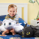 Little boy smiling while hugging the Light Fury Pillow Pet, with the Toothless Pillow Pet beside them on the bed.