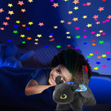 Child cuddling the Toothless Sleeptime Lite while smiling and looking up at the colorful stars projected onto the ceiling.