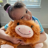 Little girl smiling while hugging the Highland Cow Pillow Pet.