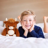 Lifestyle image of the cute brown Charlie the Highland Cow Boomeez front view next to a little boy smiling