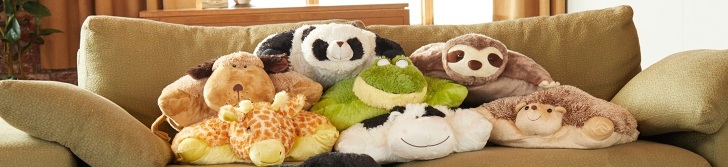 A lifestle image of seven cute and comfy Pillow Pets laying on top of each other on a couch looking forward.