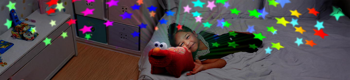 A little girl with an Elmo Sleeptime Lite on her bed, with her room all lit up with colorful rainbow stars.