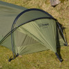 Snugpak Stratosphere Bivvi olive head end exterior view showing overlapping aluminum pole structure, Snugpak and Stratosphere branding on shelter body, No-See-Um mesh entry panel, and alloy Y-stakes staked into grass