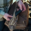 Vertx Siege 15L Sling Pack VTX5306 coyote brown close-up of hands in flannel shirt accessing rear rapid access zipper compartment showing half-pull tab detail against padded back panel