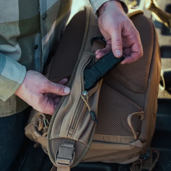 Vertx Siege 15L Sling Pack VTX5306 coyote brown close-up of hands in flannel shirt accessing rear rapid access zipper compartment showing half-pull tab detail against padded back panel