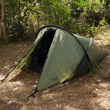 Snugpak Scorpion 2 IX olive tent deployed in wooded campsite showing fly-first pitch with door panel open revealing No-See-Um mesh inner tent and front porch storage area with gear visible inside