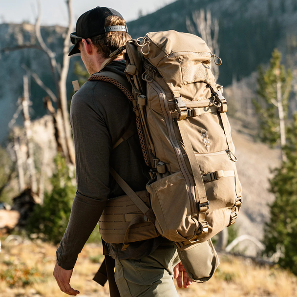 Rear carry view of Eberlestock Brute 3500 pack worn by hunter in mountain terrain with padded shoulder harness and hip belt.