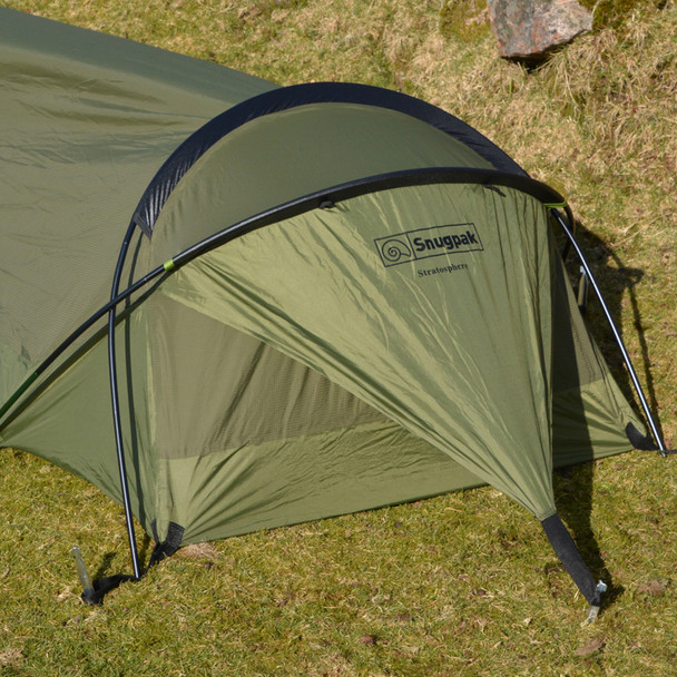 Snugpak Stratosphere Bivvi olive head end exterior view showing overlapping aluminum pole structure, Snugpak and Stratosphere branding on shelter body, No-See-Um mesh entry panel, and alloy Y-stakes staked into grass