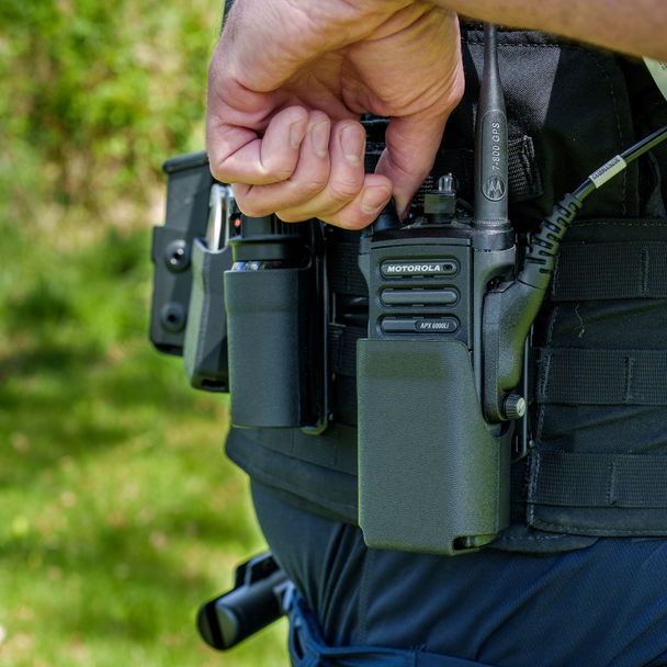 Close-up of a hand adjusting volume of a Motorola radio from the Zero9 case worn on a duty belt outdoors