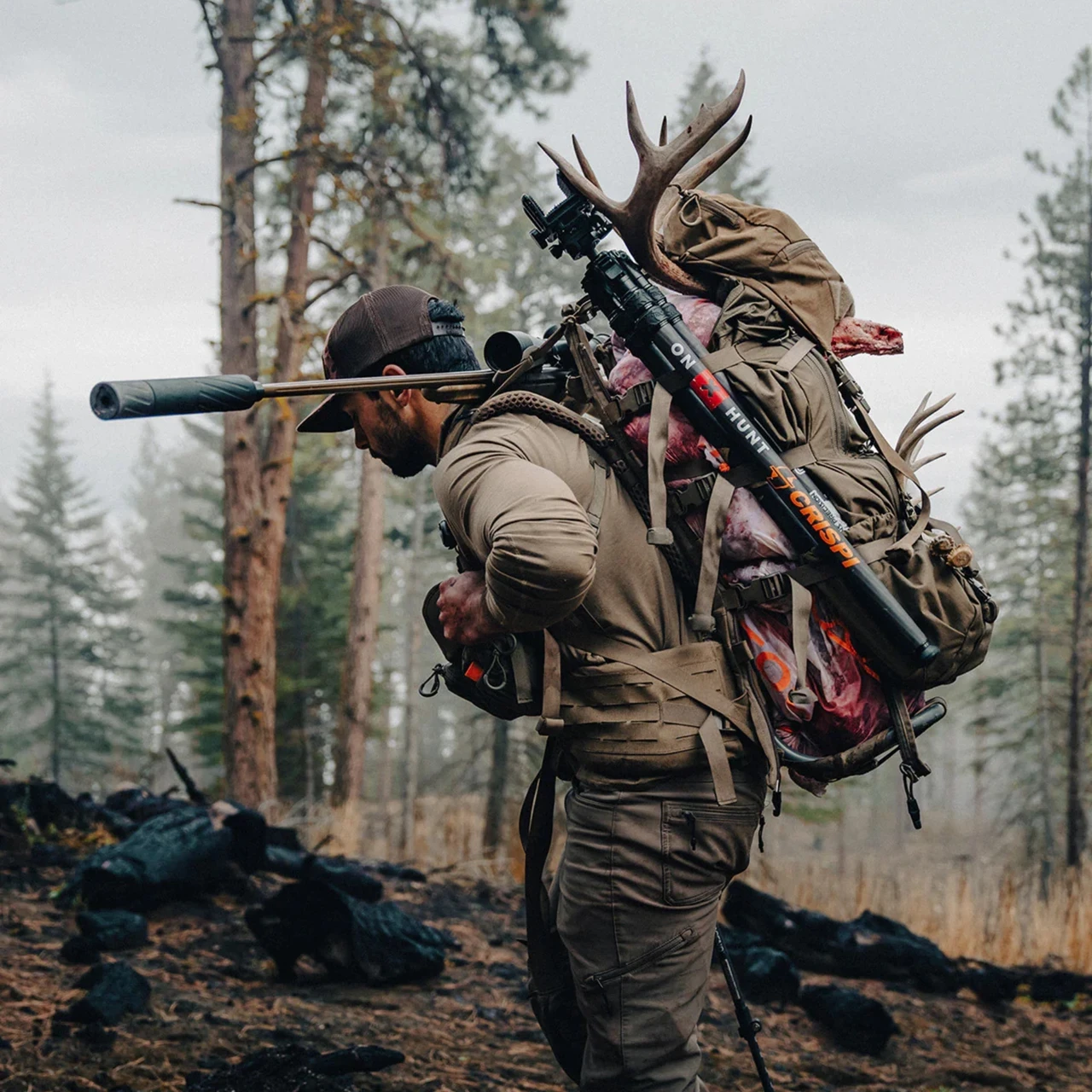 Hunter carrying a loaded frame pack with meat and antlers through a burned forest