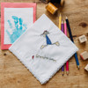 Embroidered kid's drawing on a white lace handkerchief. Embroidery is sewn in blue, black, yellow and red thread. Shown with color pencils, stamps, threads and kid's handprint painting for decoration.