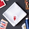 White handkerchief embroidered with a small lobster in red thread in the corner. Handkerchief shown on gray background with stamps and thread.