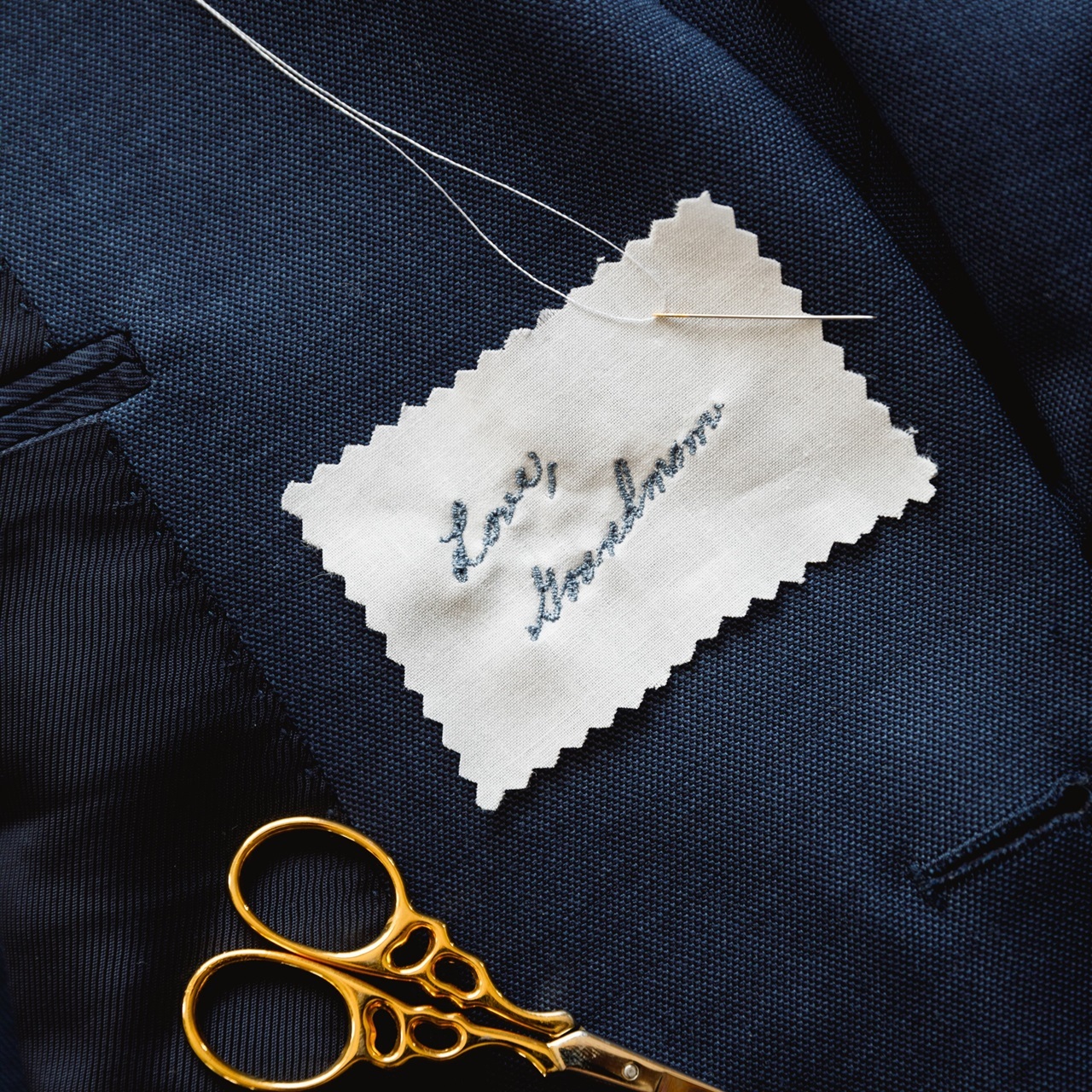 Handwritten embroidered swatch for suit or dress. Shown in blue thread on a men's suit.