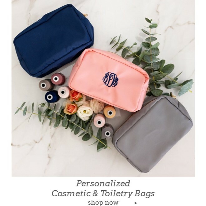 Personalized monogrammed cosmetic bags in pink, navy and gray. Shown with navy embroidery thread. Flowers and spools of thread for decor.