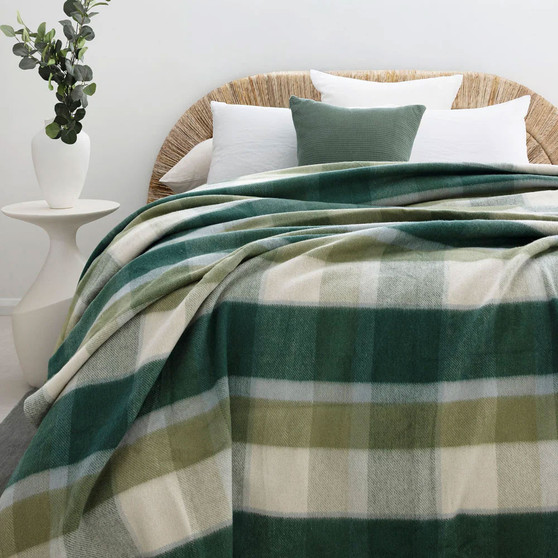 Green check wool‑bamboo blanket styled on a bed with white pillows and a plant in the background.