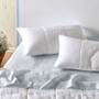 Linen House Nimes White Pillowsham pair styled on bed with light blue sheets