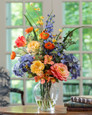 Gorgeous Painter's Palette Silk Flower Arrangement in Yellow Orange designed in a 7" jardin vase of crystal clear acrylic water