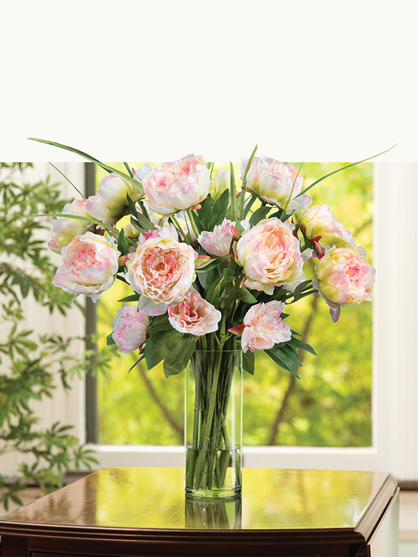 Faux floral arrangement with mixed roses in peach, red, and cream tones displayed in a clear glass vase